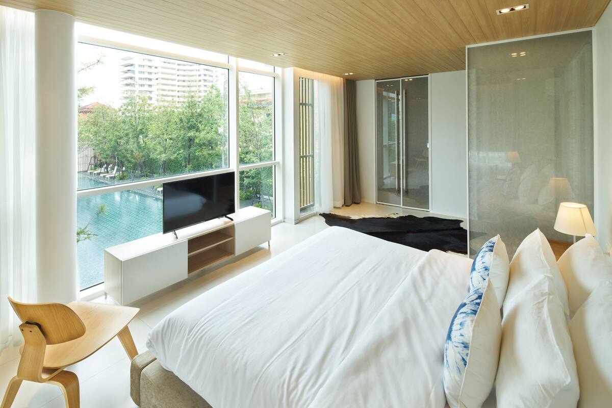 A modern hotel room with a large bed, a TV, a view of a swimming pool, and a balcony.