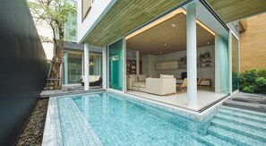 A modern house with a swimming pool, a glass door leading to a living room with a sofa and a TV, and a wooden ceiling.