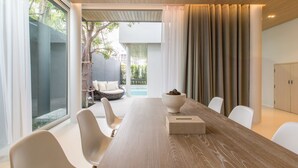 A modern meeting room with a long wooden table, white chairs, and a view of an outdoor seating area with a pool. - Veranda Residence Pattaya Pool Villa (Pattaya)
