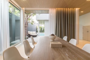 A modern meeting room with a long wooden table, white chairs, and a view of an outdoor seating area with a pool.