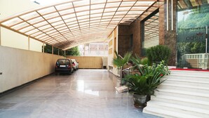 A covered parking area with a car, potted plants, and a building entrance.