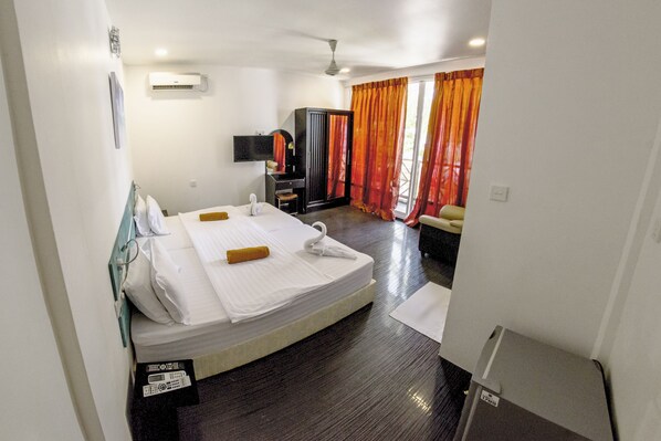 Habitación de hotel con cama, escritorio, televisor y balcón con cortinas.
