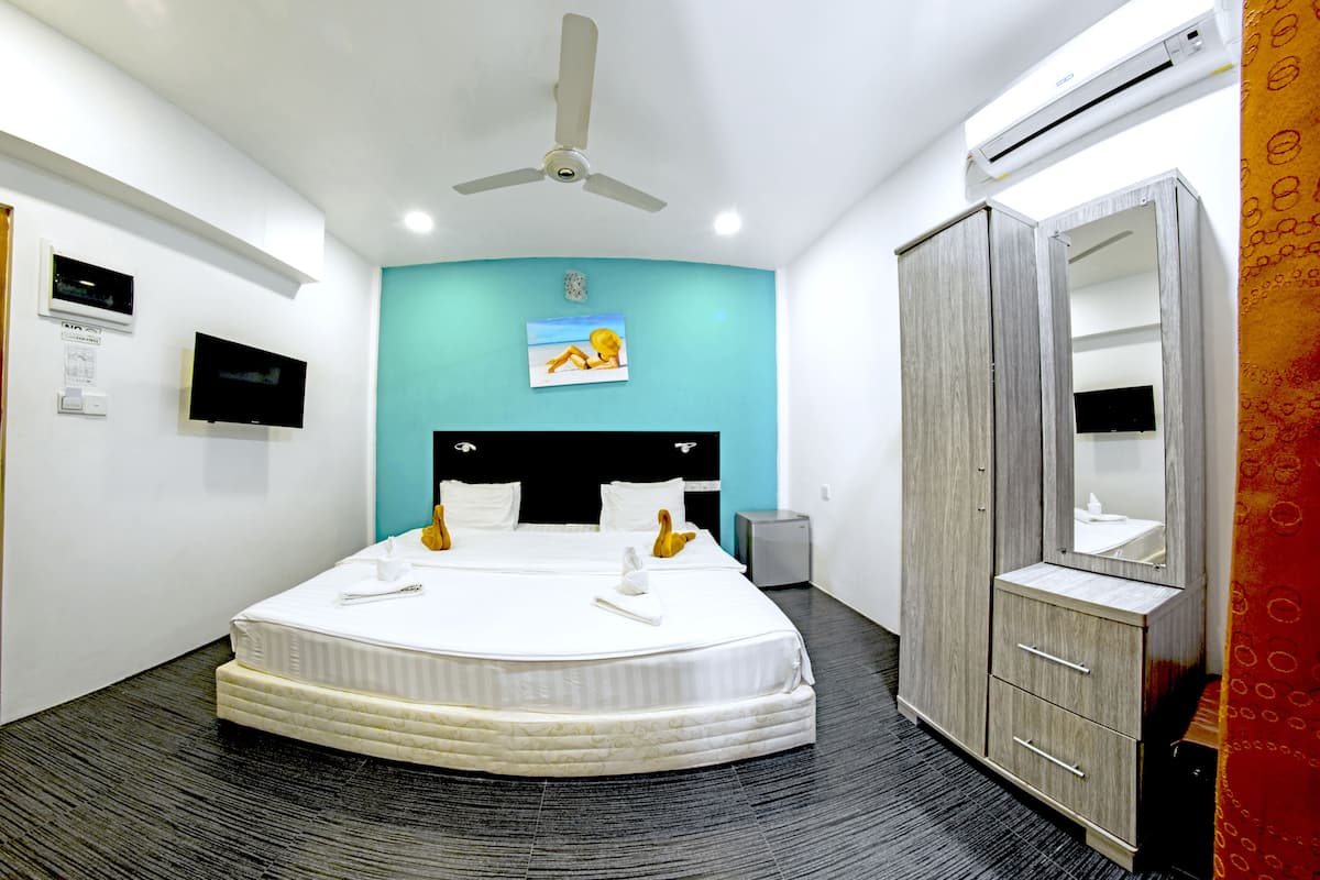 A hotel room with a bed, a ceiling fan, an air conditioning unit, a television, and a wardrobe.