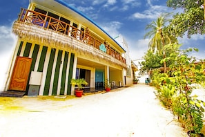 A two-story building with a balcony, potted plants, and a palm tree.