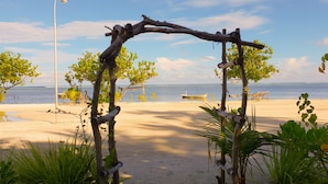 Una spiaggia con un arco in legno, palme e vista libera sull'oceano.
