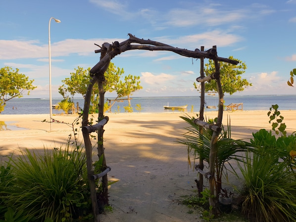 A beach with a wooden archway, palm trees, and a clear view of the ocean.