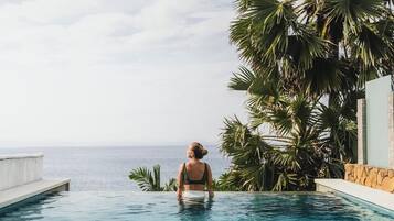 Una mujer en una piscina con vista al mar y palmeras.