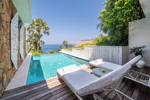 Un área junto a la piscina con muelle de madera, sillas de descanso y vista al océano.