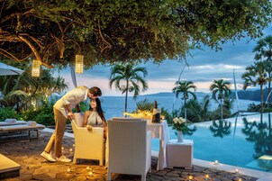 Un espacio de comedor al aire libre con vista al océano, una piscina y palmeras.