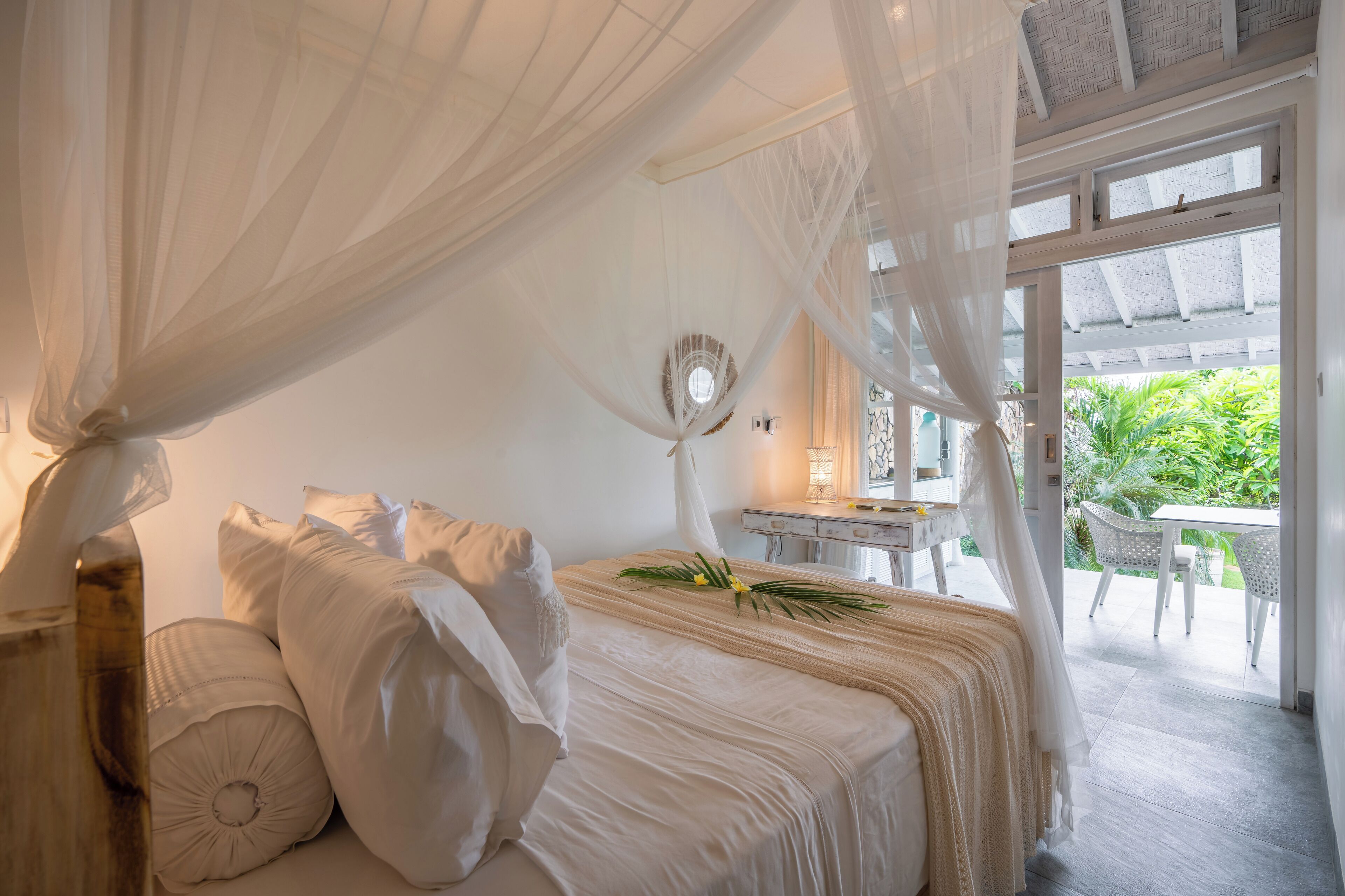 A bedroom with a canopy bed, a desk, and a view of the outdoors.