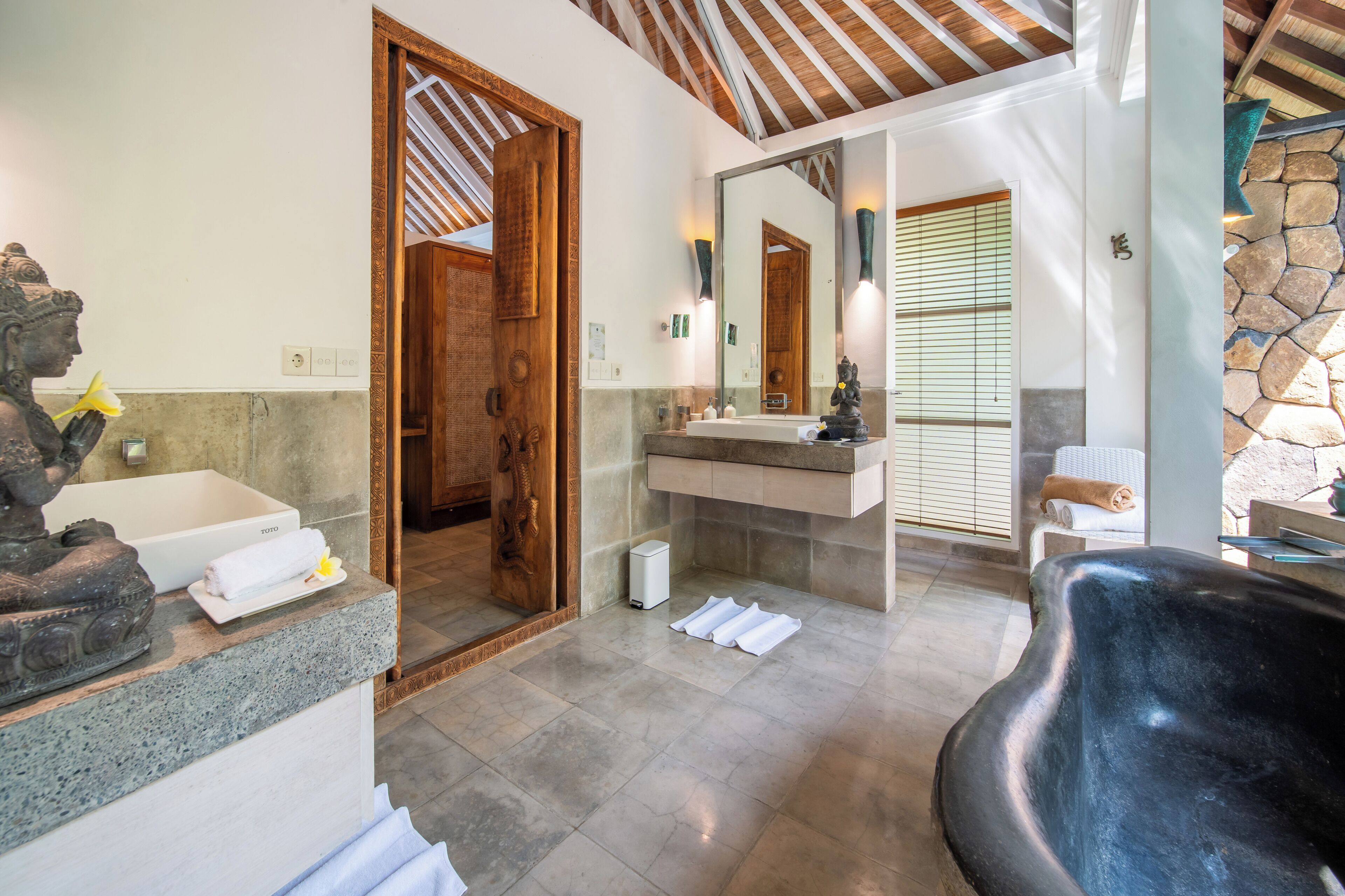 A bathroom with a bathtub, a sink, and a mirror. There is a statue on the counter and a towel on the floor.