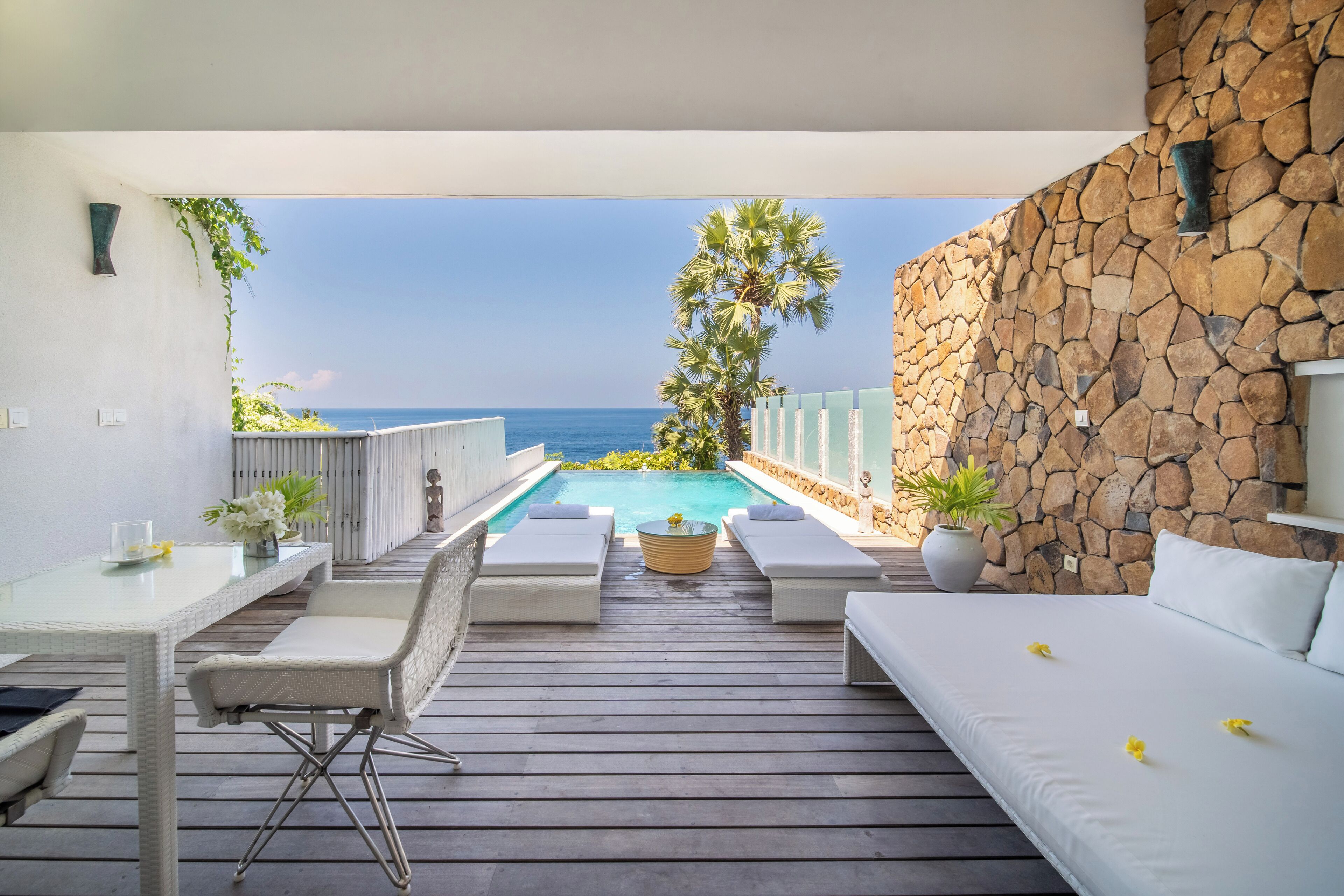 A balcony with a pool, white furniture, and a stone wall.