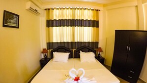 A double bed with a heart-shaped towel arrangement, a dark headboard, and a black wardrobe.