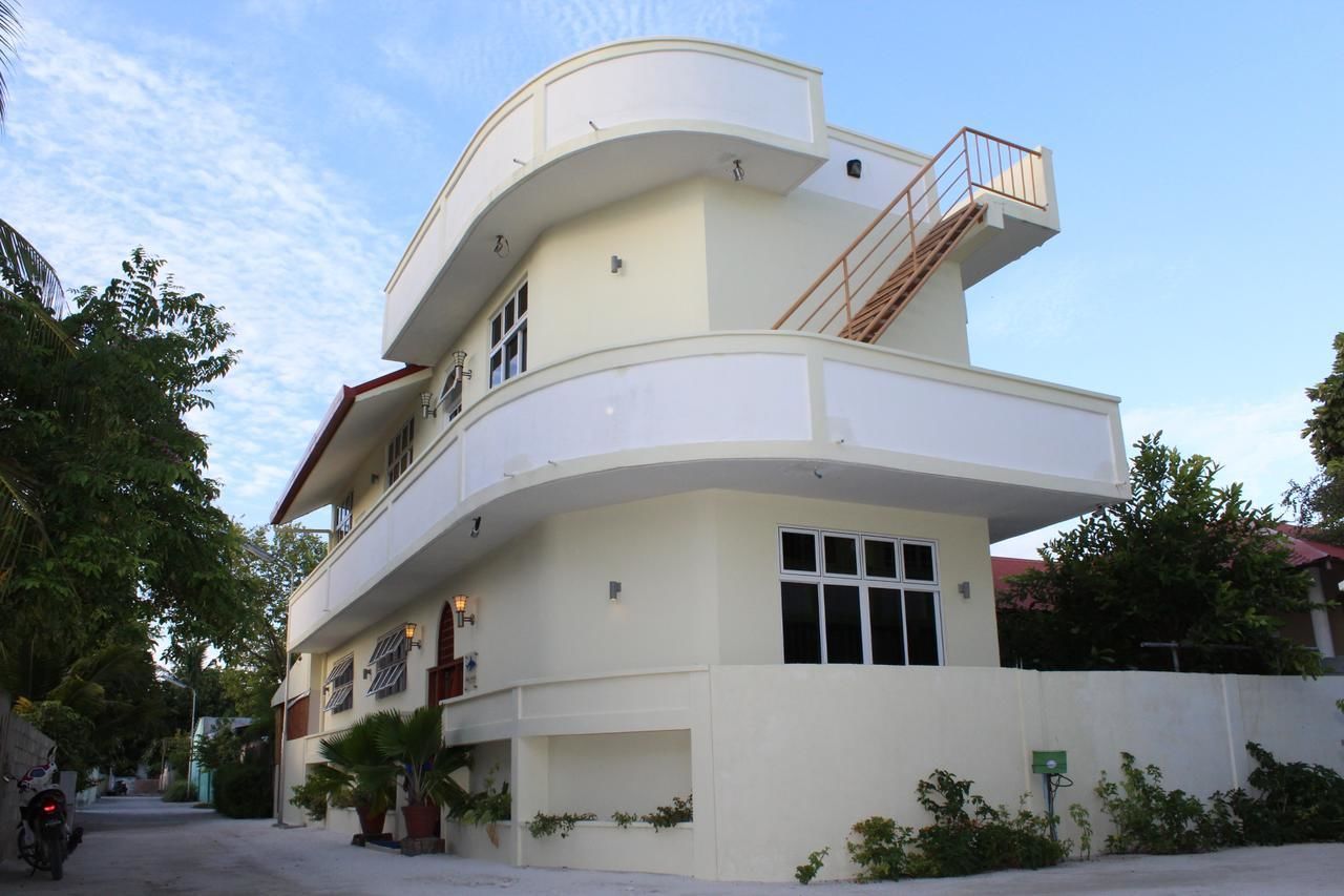 A modern, multi-story building with a curved facade, a balcony on the upper floor, and a staircase leading to the entrance.