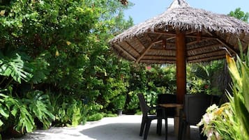 Un espace extérieur aménagé avec des sièges et une table, doté d’un toit de chaume et entouré d’une végétation luxuriante.