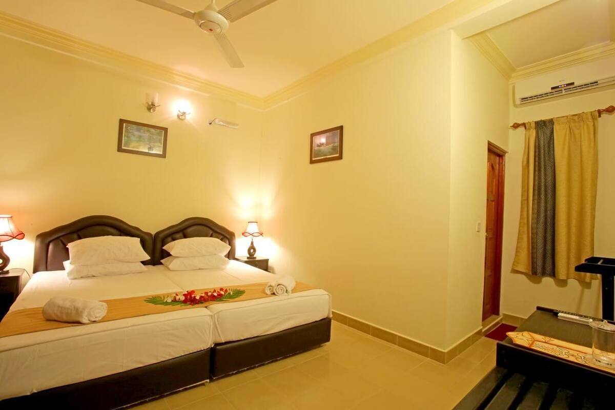 A hotel room with a double bed, bedside lamps, a ceiling fan, and a small table with a glass.