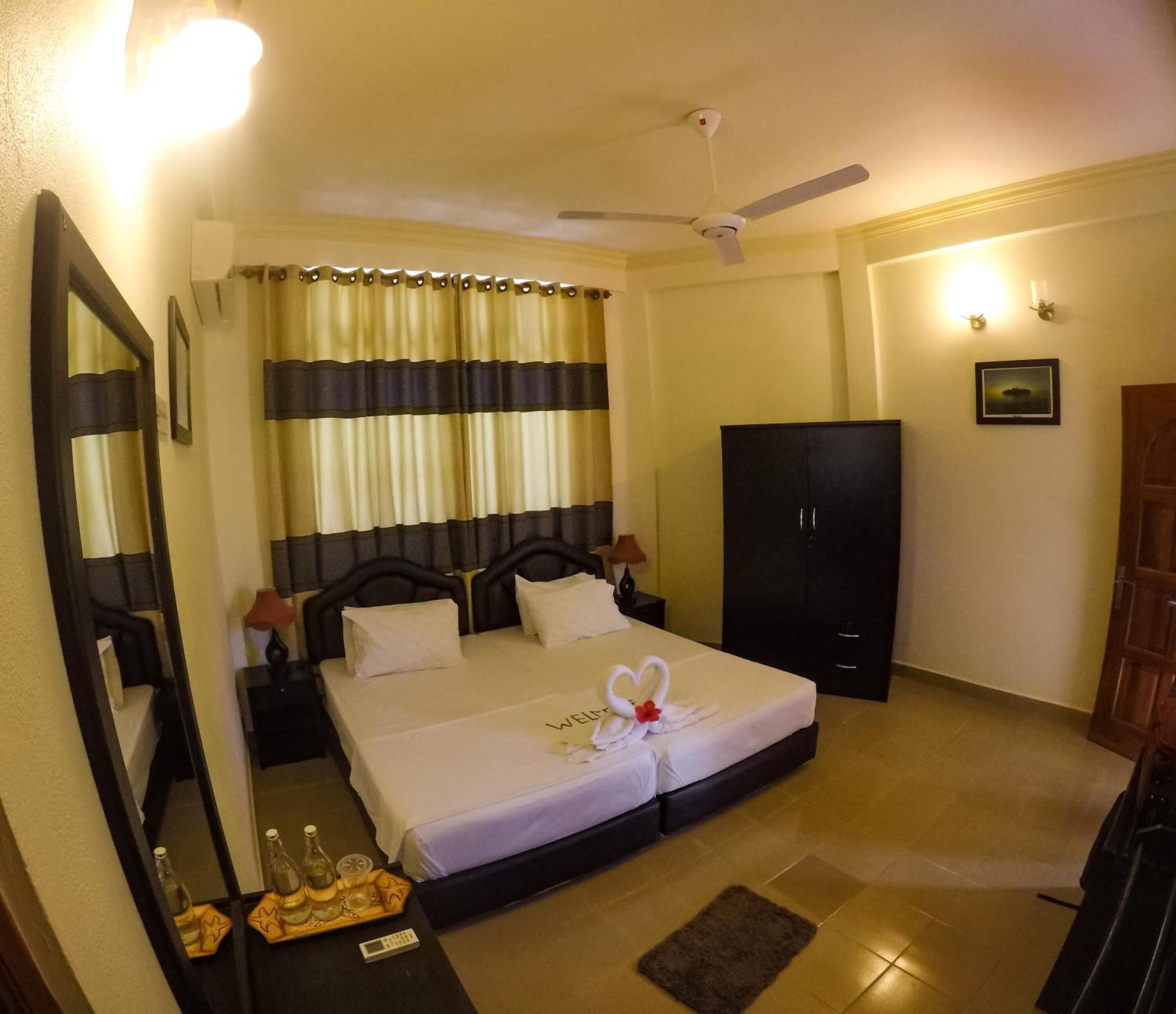 Une chambre d’hôtel avec deux lits, une armoire, un ventilateur de plafond et un miroir.