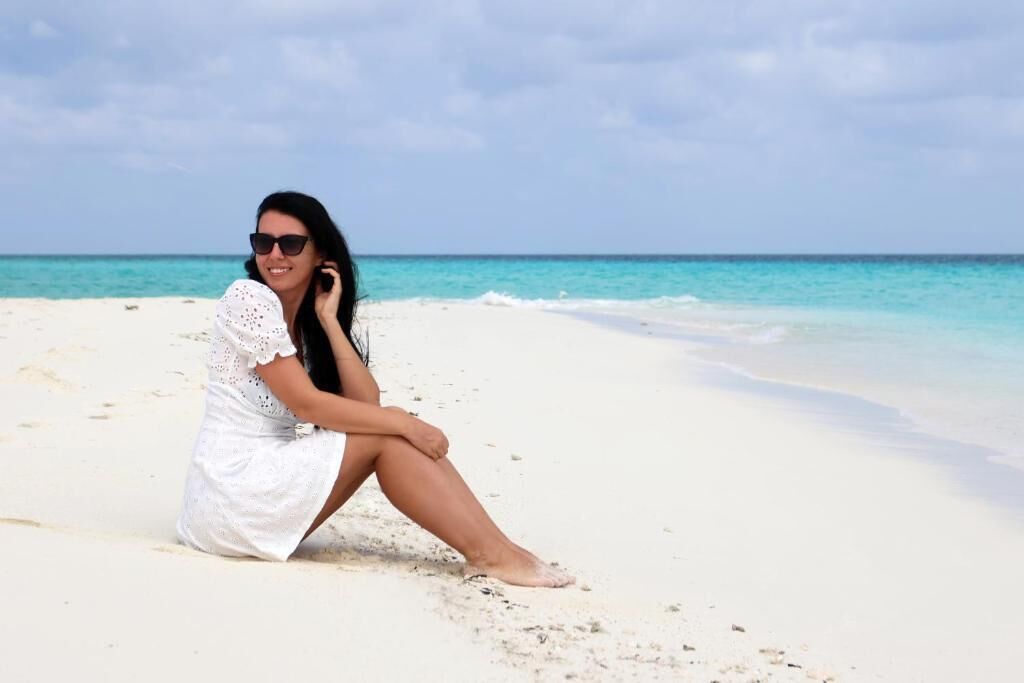 Una persona seduta su una spiaggia sabbiosa, con un cielo sereno e un mare calmo sullo sfondo.