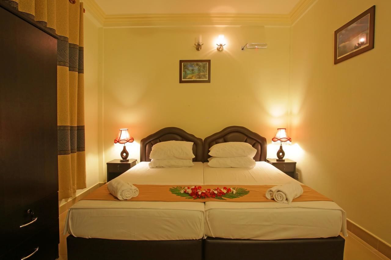 Una cama doble con dos mesitas de noche, cada una con una lámpara, en una habitación con paredes color crema y un cuadro enmarcado sobre la cama.