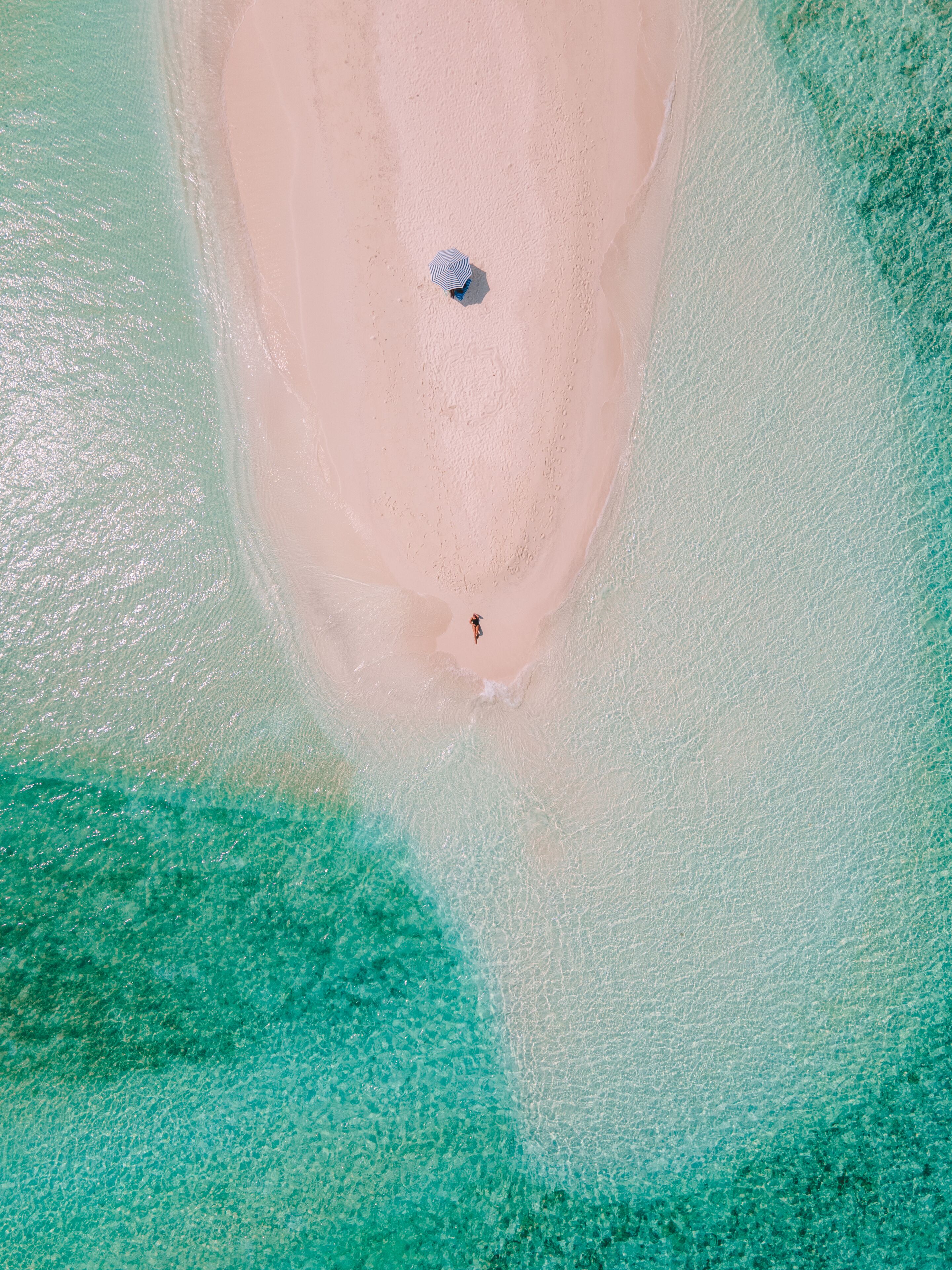 En vy över en strand sedd från luften, med kristallklart turkosfärgat vatten och en sandstrand.