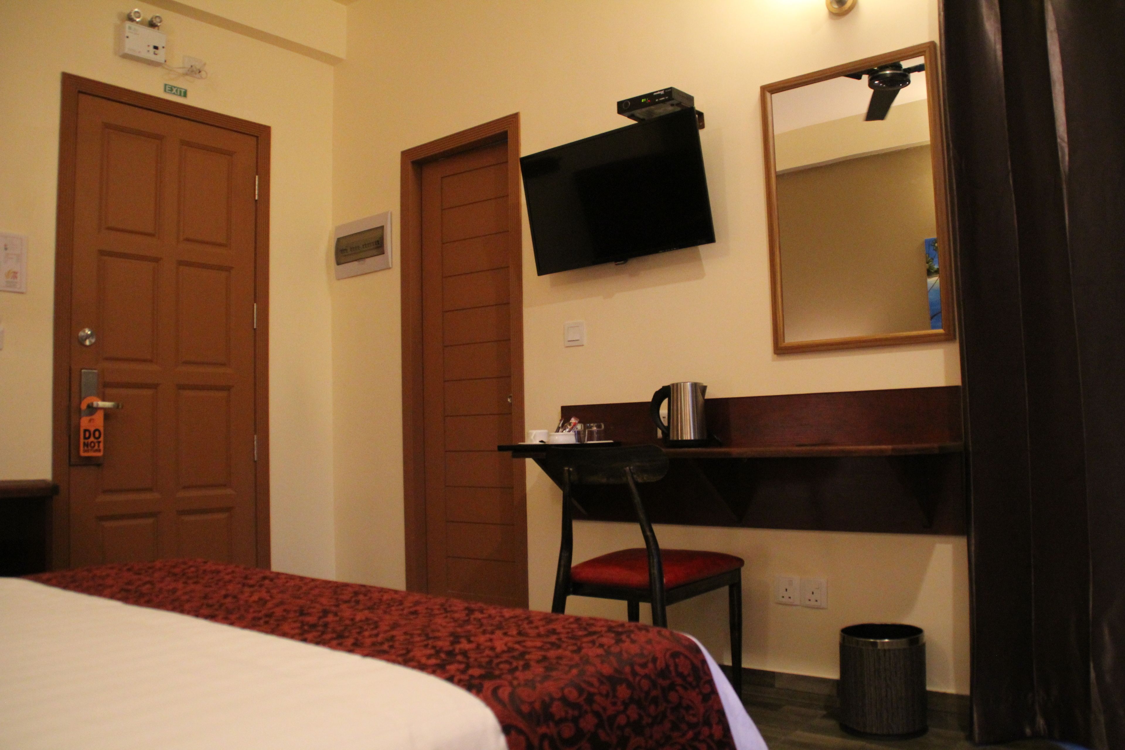 Ein Hotelzimmer mit Bett, Schreibtisch mit Stuhl, Wandfernseher und Spiegel.
