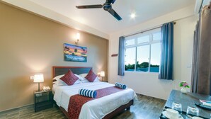 A hotel room with a large bed, a ceiling fan, a window with curtains, a bedside table with a lamp, and a tray with cups and glasses.