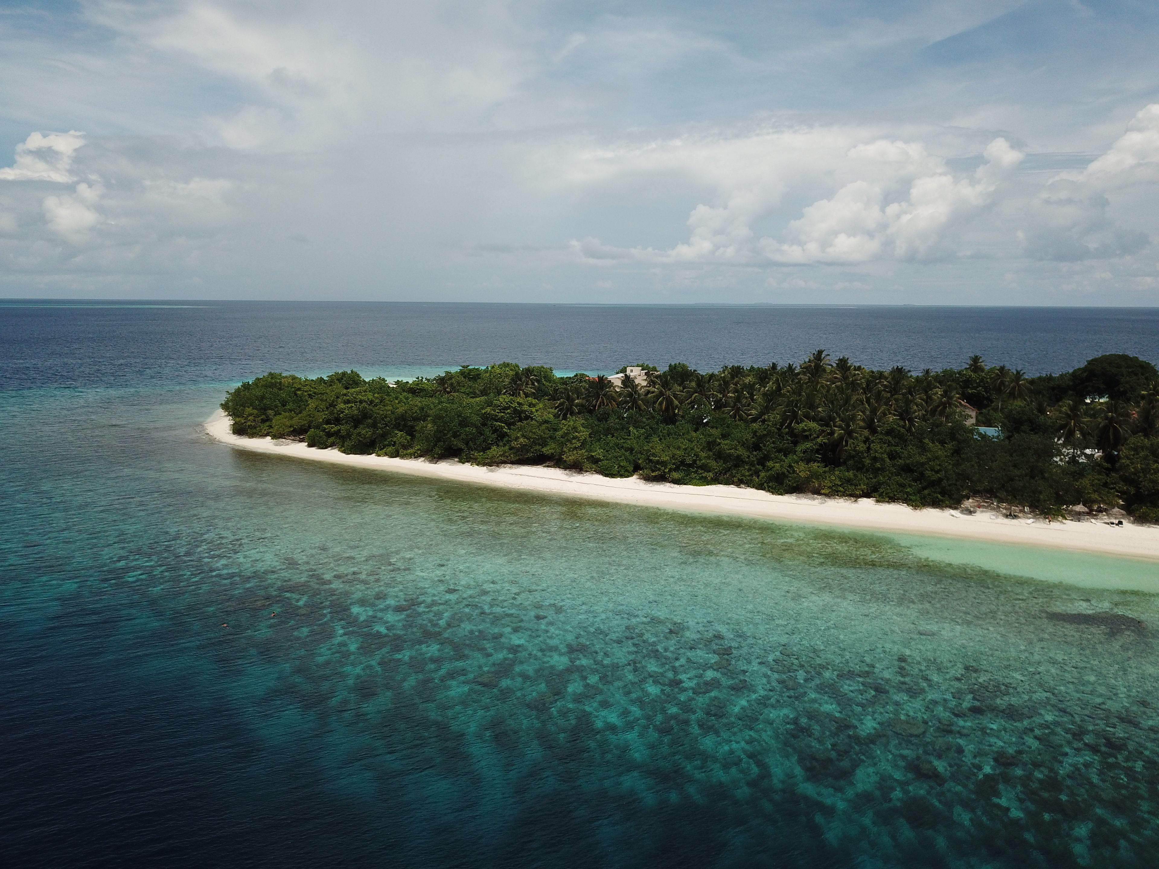 An aerial view of a tropical island with a white sandy beach, dense green vegetation, and clear turquoise waters.