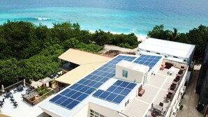 A building with solar panels on the roof, a pool area, and a view of the ocean.