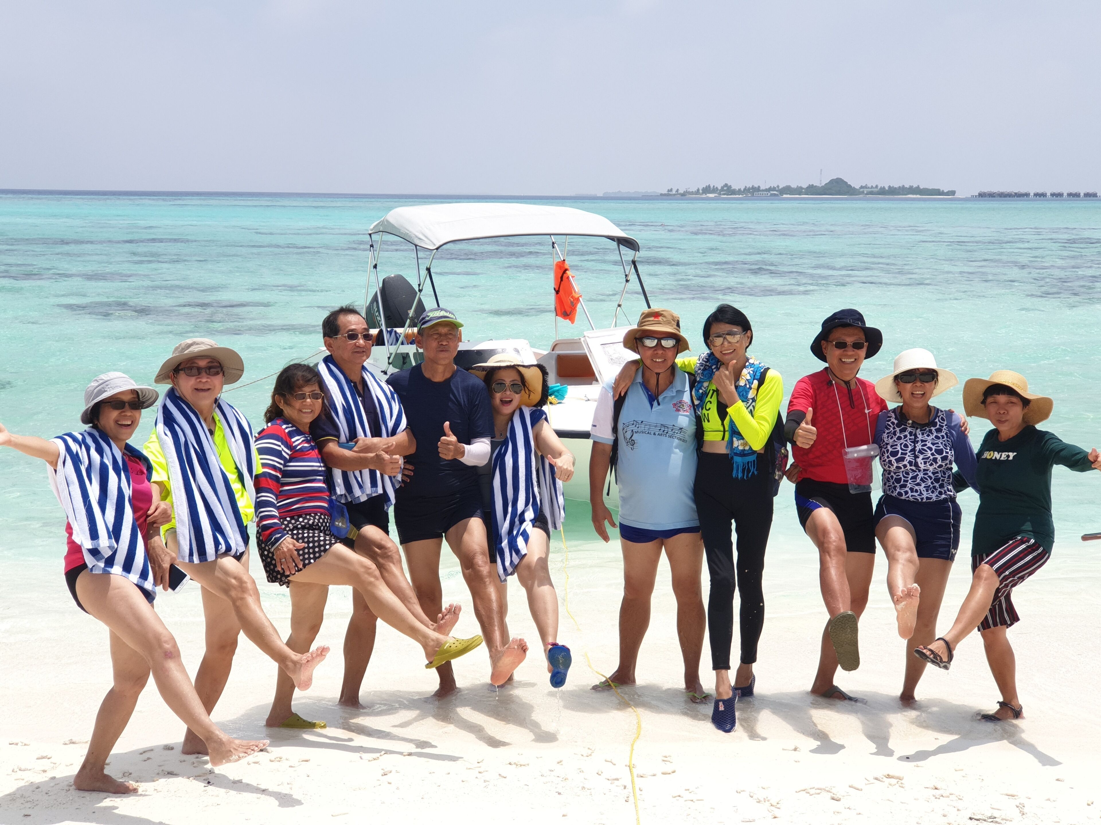 A group of people on a beach with a boat in the background.
