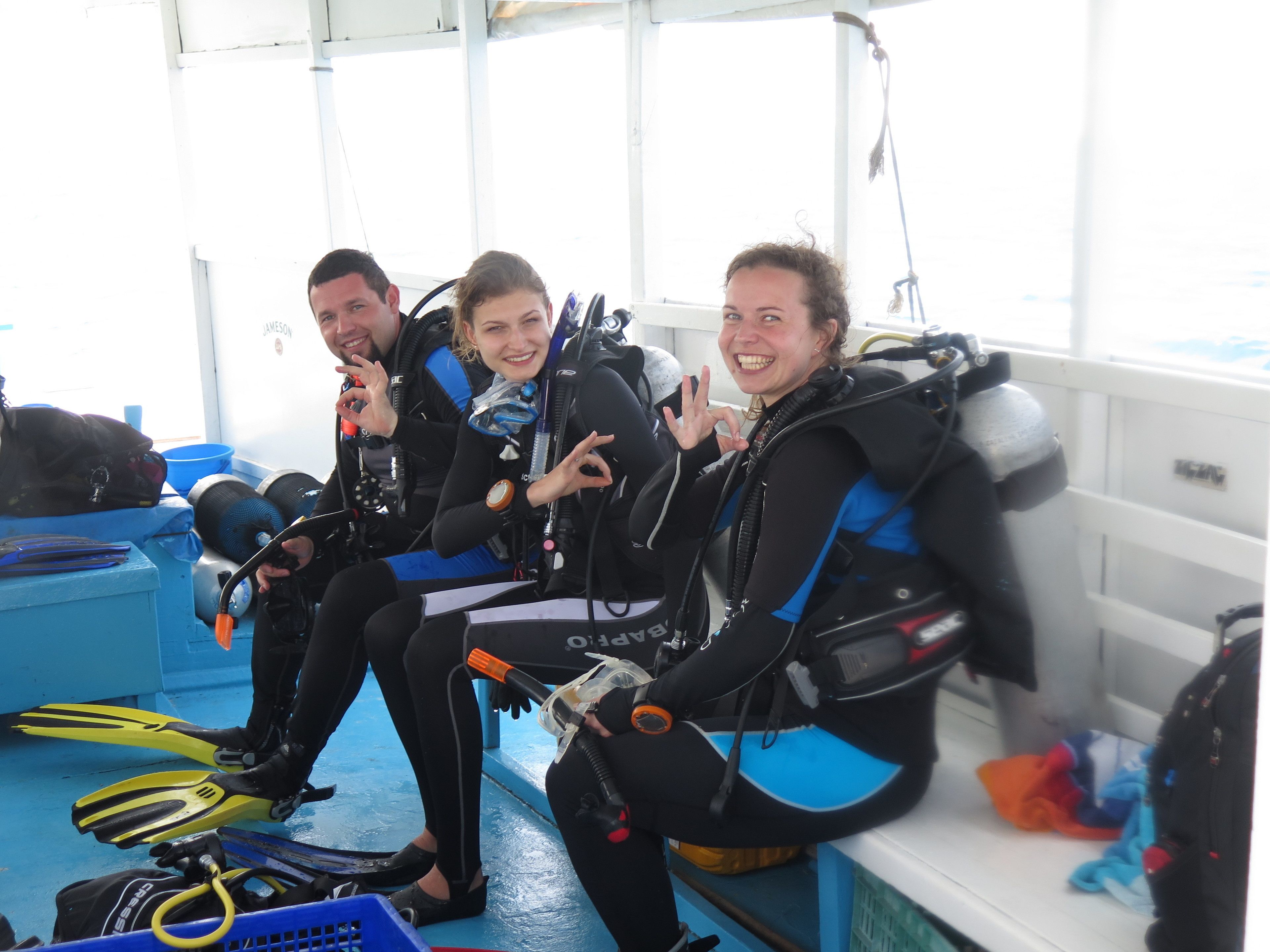 Tres personas con equipo de buceo sentadas en un banco, con equipo de buceo a su alrededor.