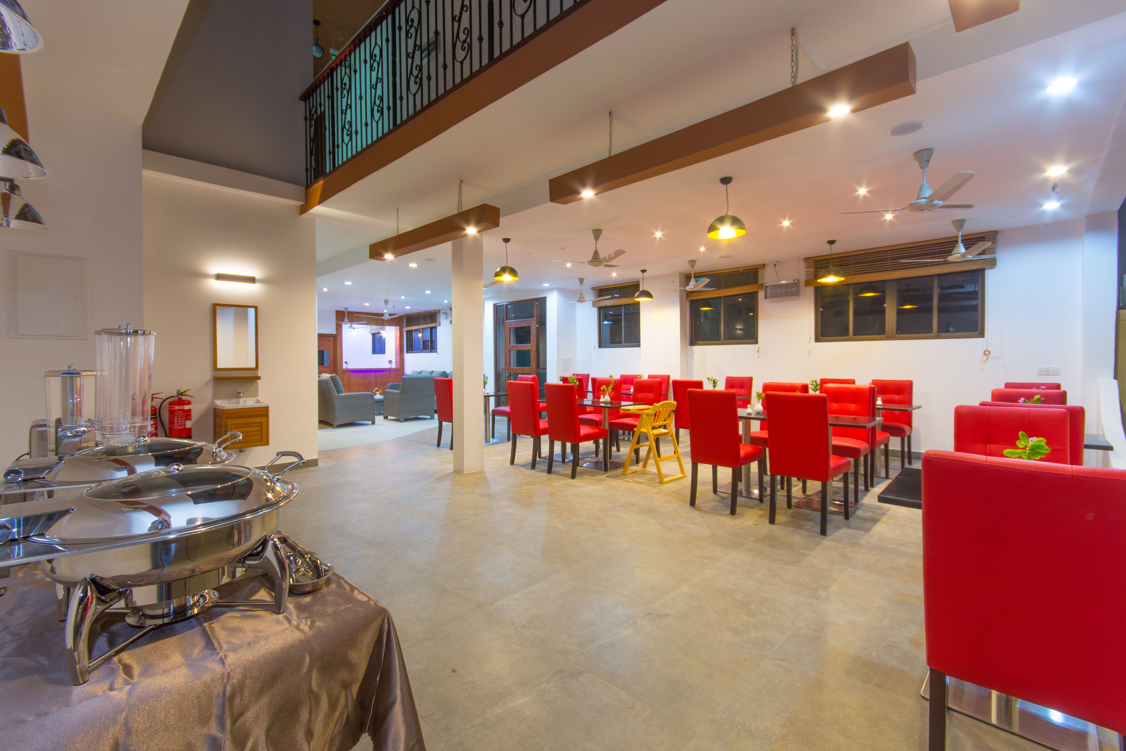 A spacious dining area with red chairs and tables, a high ceiling with multiple light fixtures, and a visible staircase.
