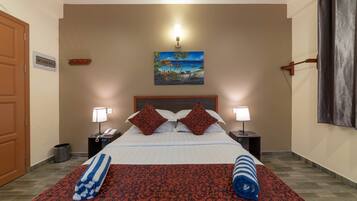 A hotel room with a bed, two bedside lamps, a painting of a beach scene, and a window with curtains.