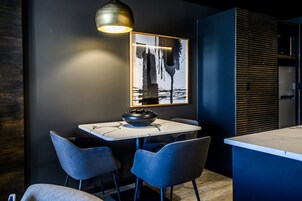 Una cocina moderna con encimera de mármol, dos sillas azules, un tazón negro y un cuadro abstracto enmarcado en la pared.
