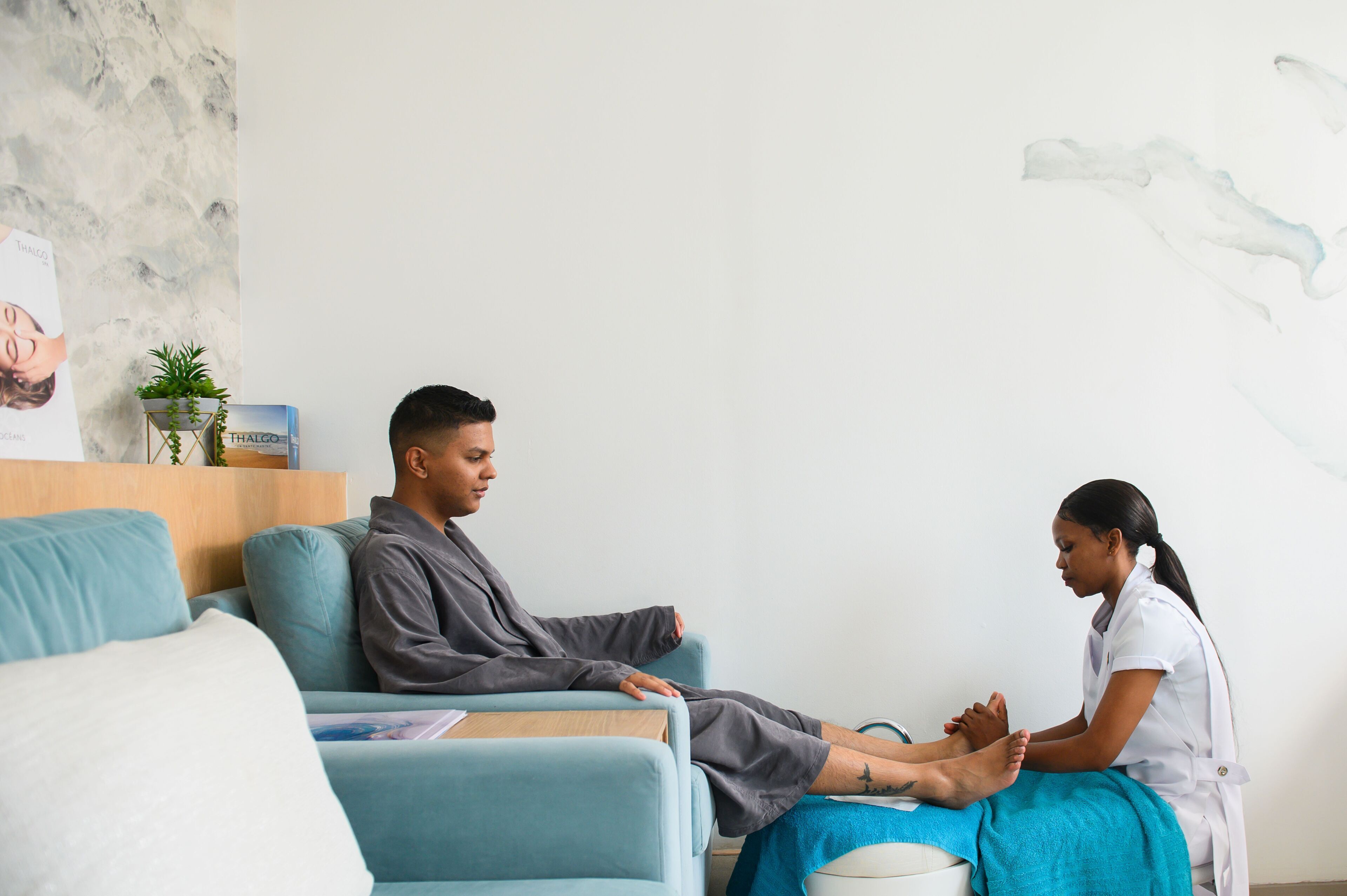 A person receiving a foot massage in a room with a blue couch, a small plant, and a poster on the wall.