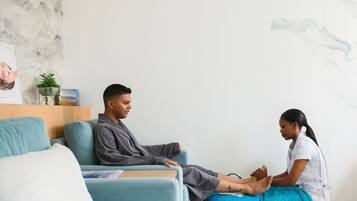 A person receiving a foot massage in a room with a blue couch, a small plant, and a poster on the wall.