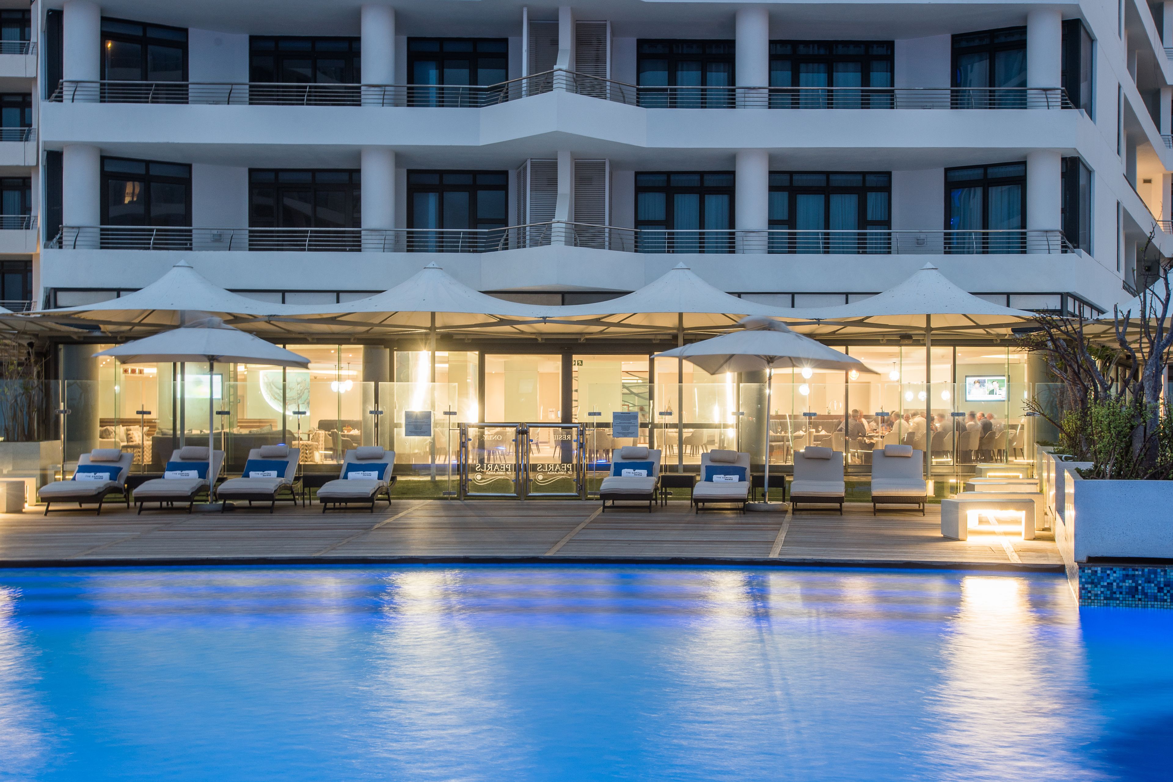 Hotel amb zona de piscina, gandules, ombrel·les i restaurant amb façana de vidre.