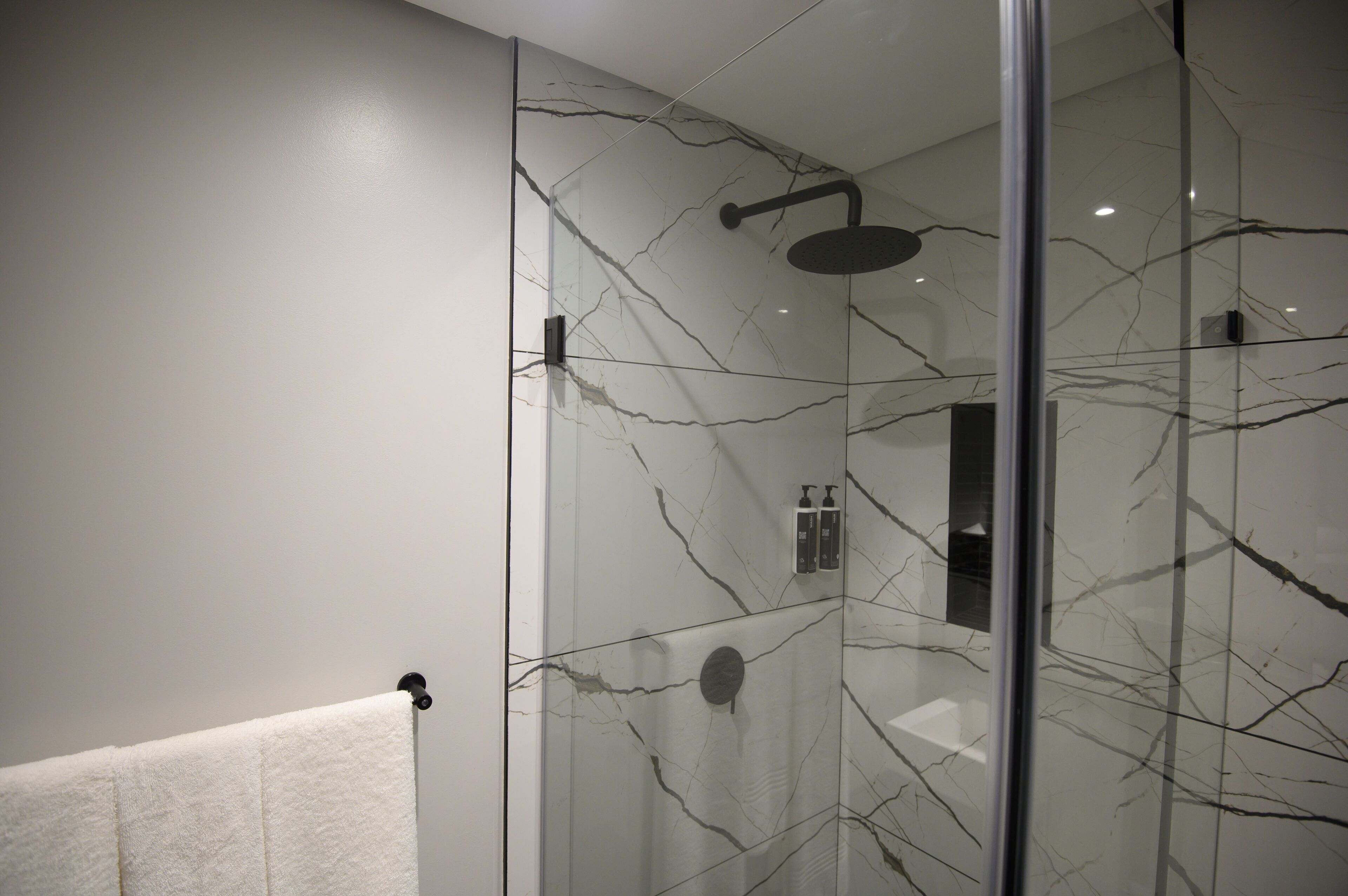 Un bany modern amb una cabina de dutxa de vidre, parets de marbre i una tovallola blanca penjada a un ganxo.