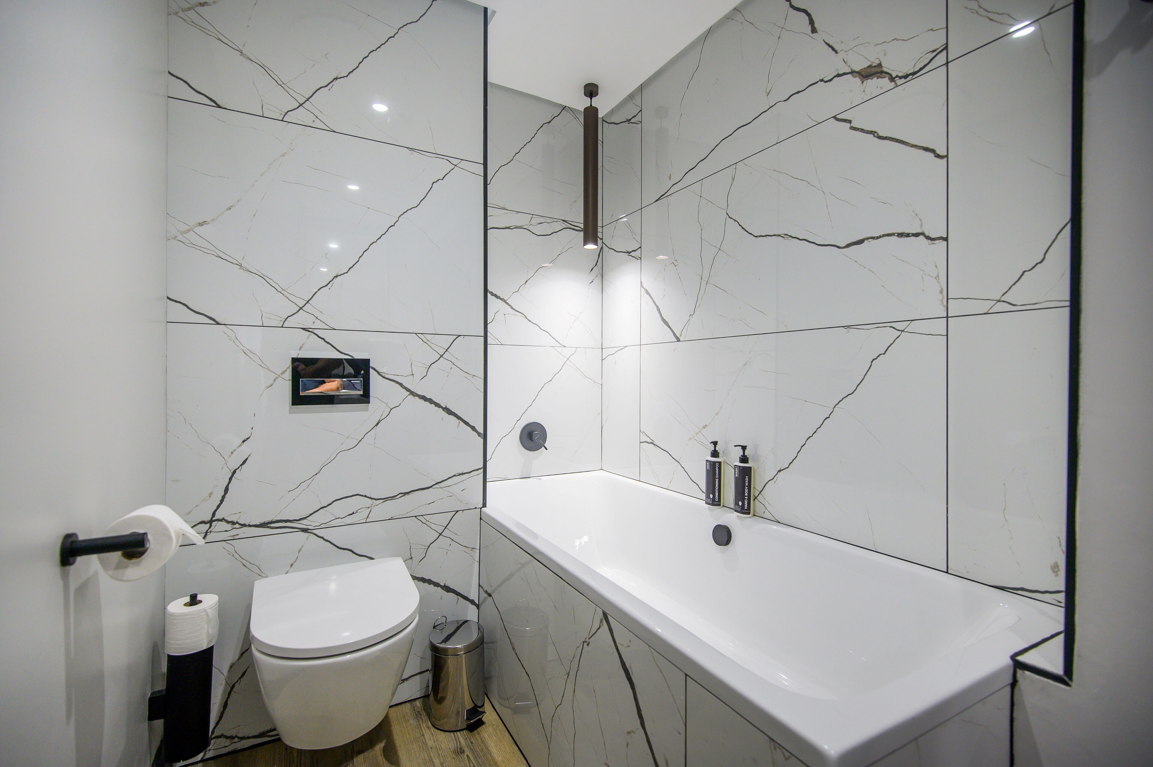 A modern bathroom with a white marble wall, a toilet, a sink, and a shower area.