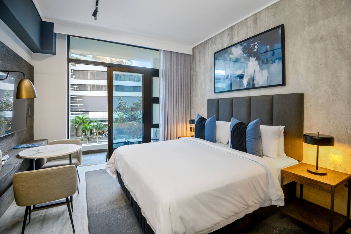 A modern hotel room with a large bed, a desk, a chair, and a view of the outside.