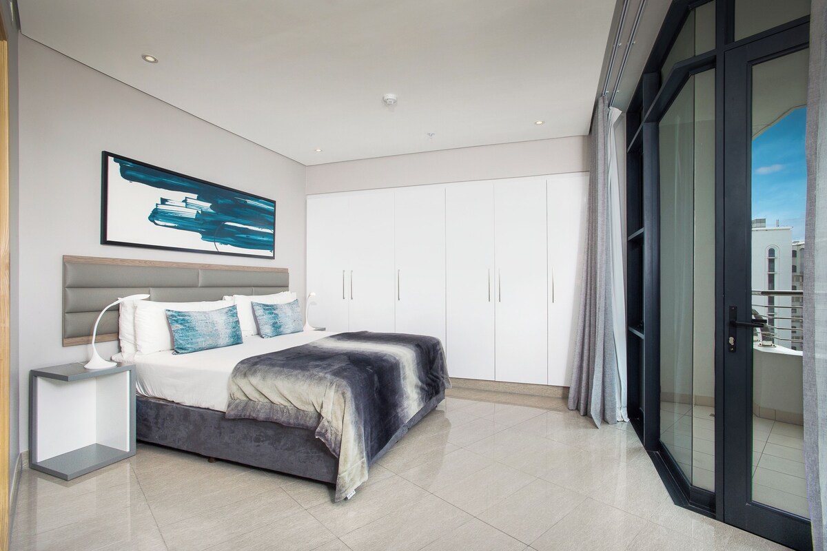 A modern bedroom with a bed, bedside table, and a large window.