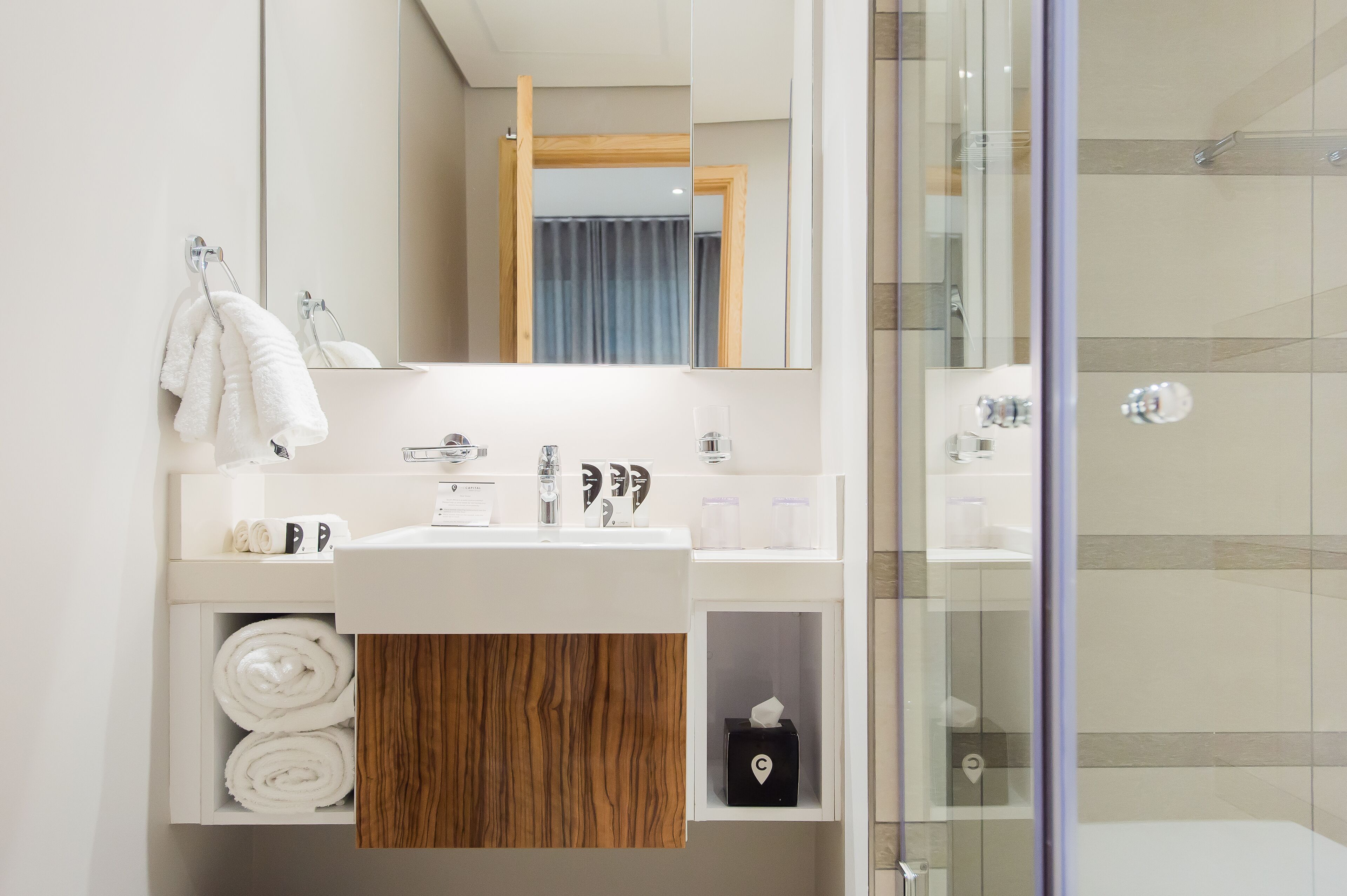 A modern bathroom with a white sink, mirror, and glass shower enclosure.