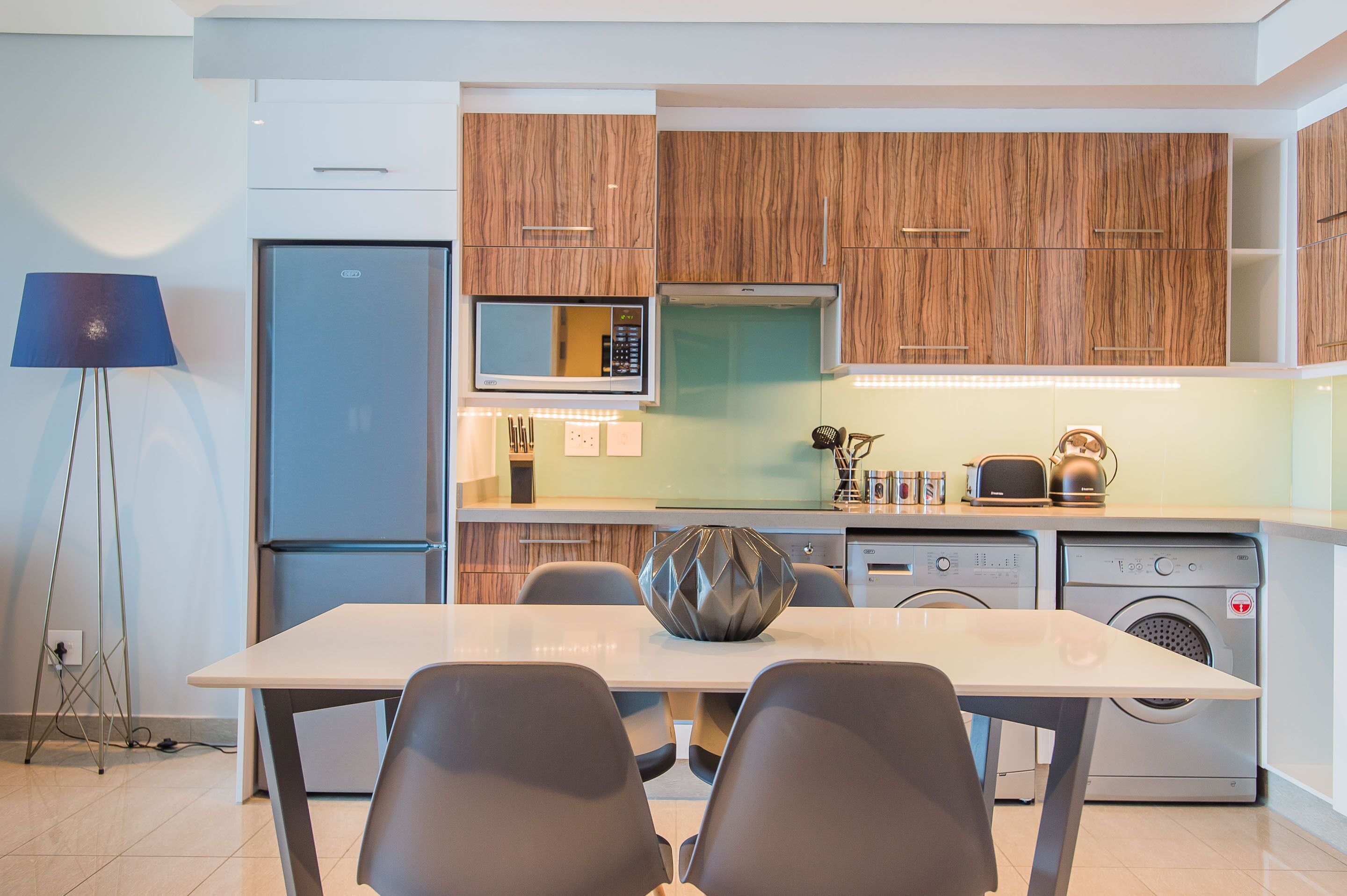 Una cocina moderna con armarios de madera, microondas integrado, hervidor y lavadora.