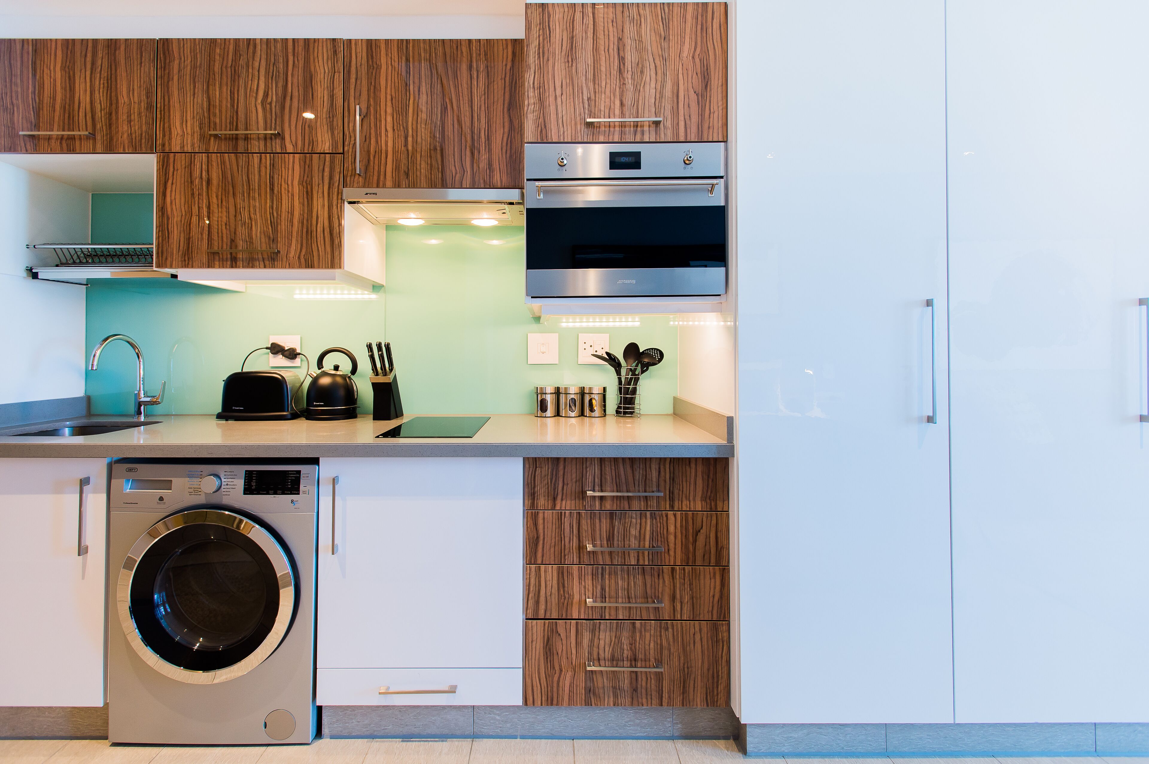 A modern kitchen with a built-in washer, a stainless steel oven, and wooden cabinetry.
