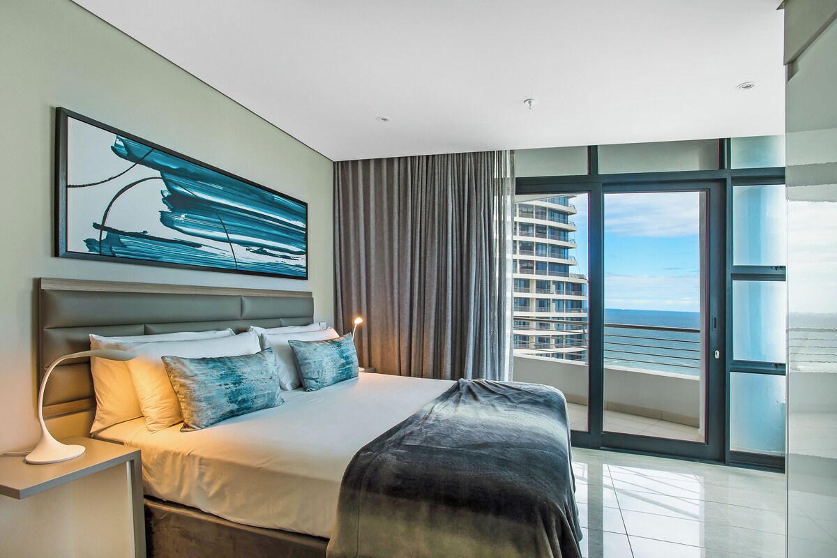 A modern hotel room with a large bed, a view of the ocean, and a balcony.
