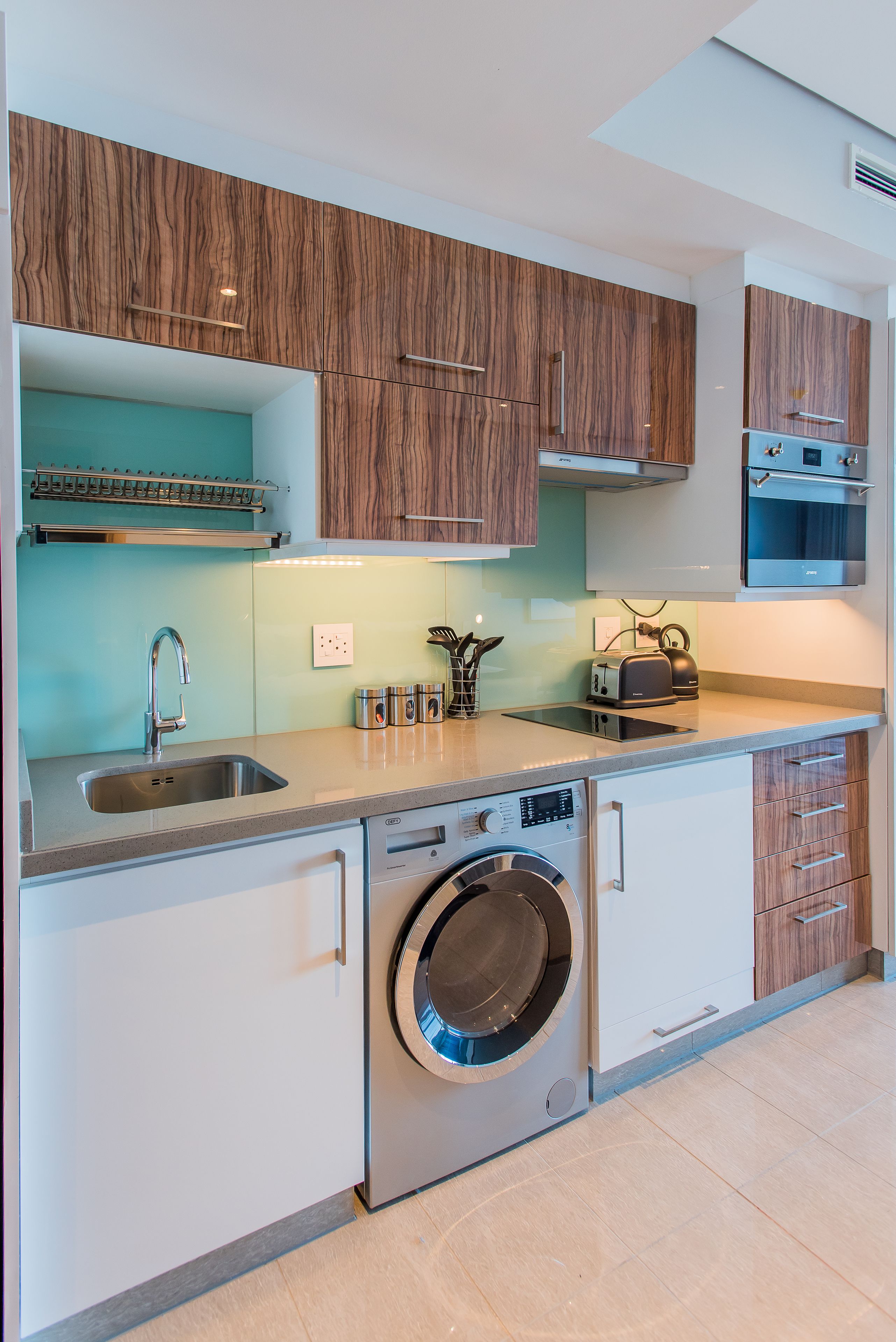 Une cuisine moderne avec des meubles en bois, un lave-linge encastré et un évier en acier inoxydable.