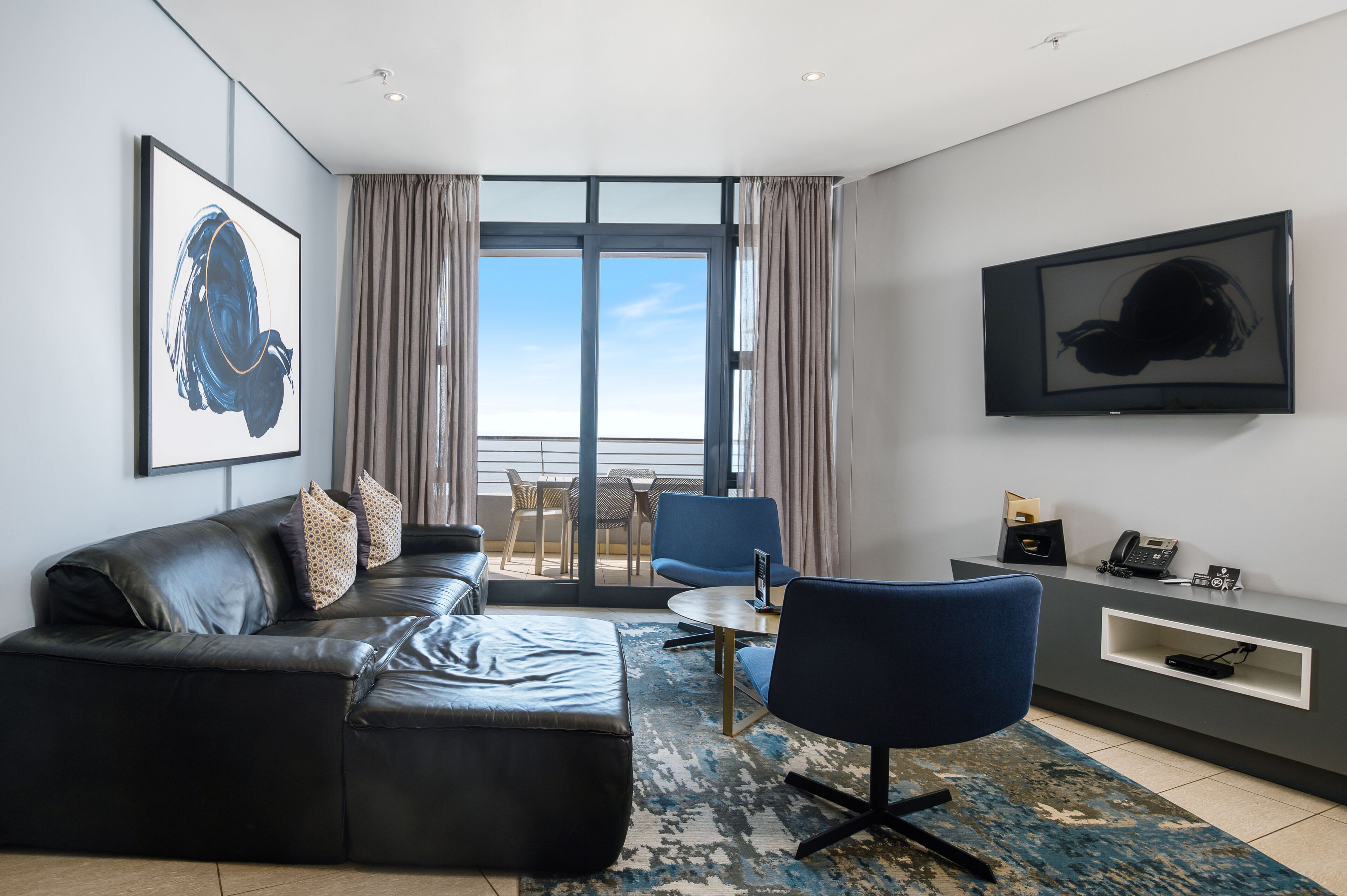 A modern living room with a leather sofa, a blue armchair, a small round table, and a TV mounted on the wall.