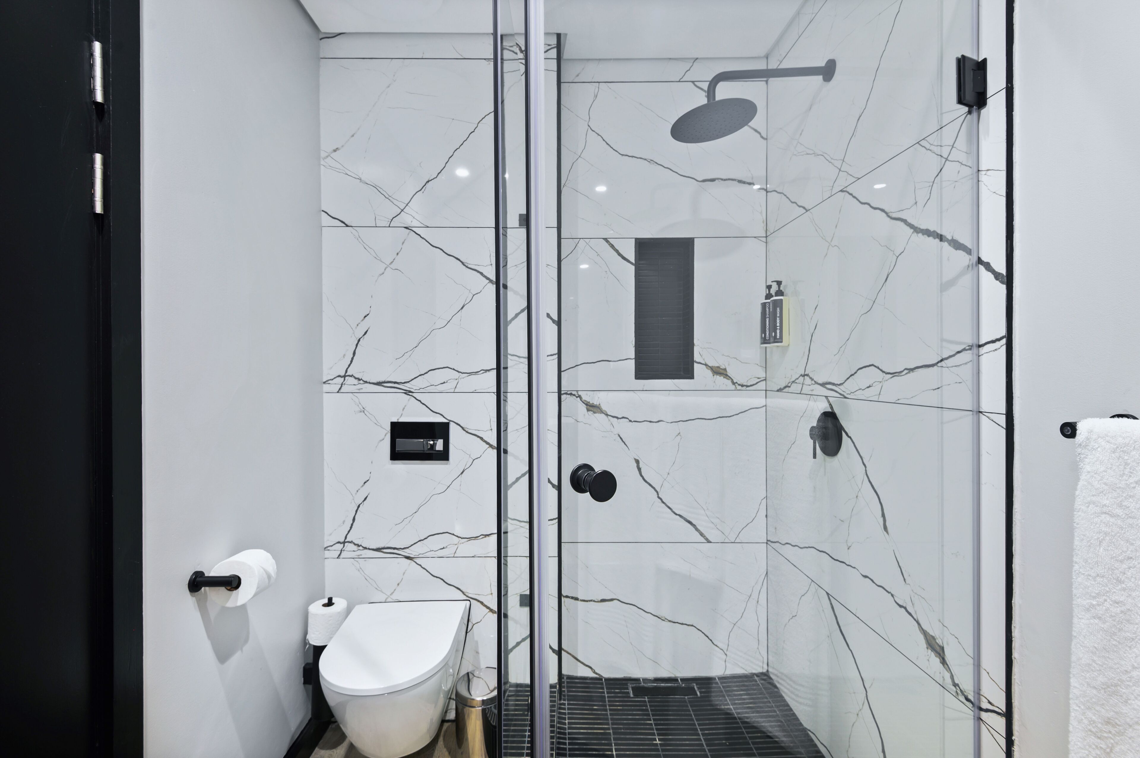 Une salle de bain moderne avec une douche à parois de verre, des toilettes blanches et un mur décoré d’un motif marbré.