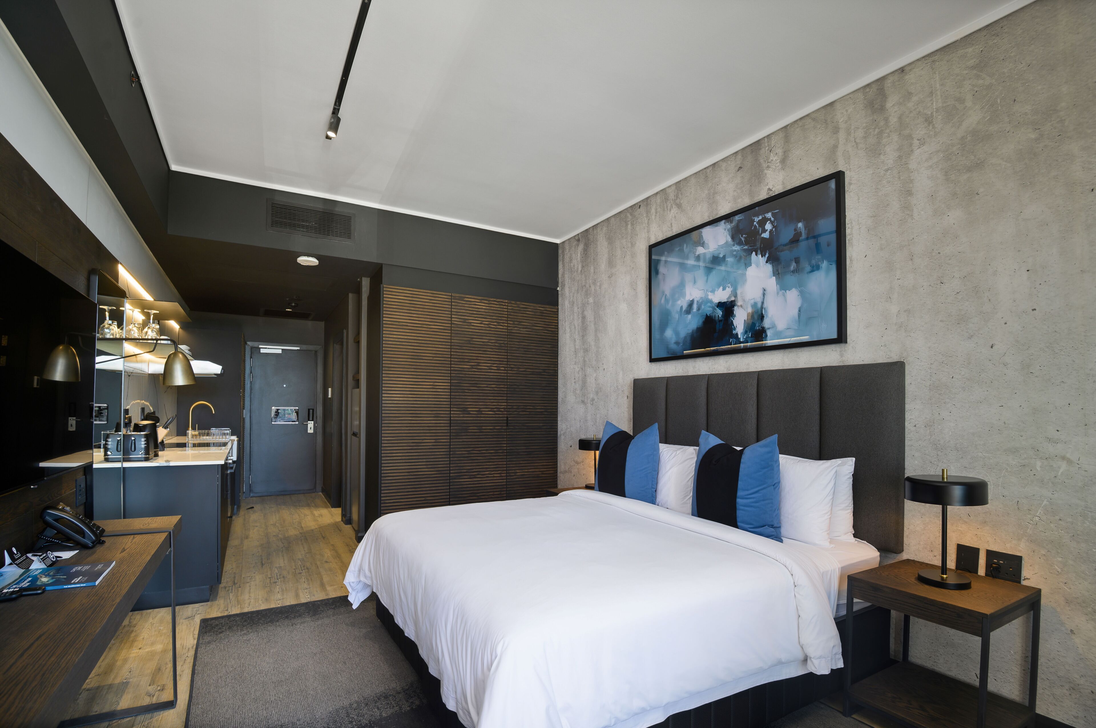 A modern hotel room with a large bed, bedside table, and a desk with a chair.