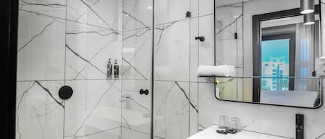 A modern bathroom with a glass-enclosed shower, a white marble backsplash, and a large mirror reflecting a cityscape.