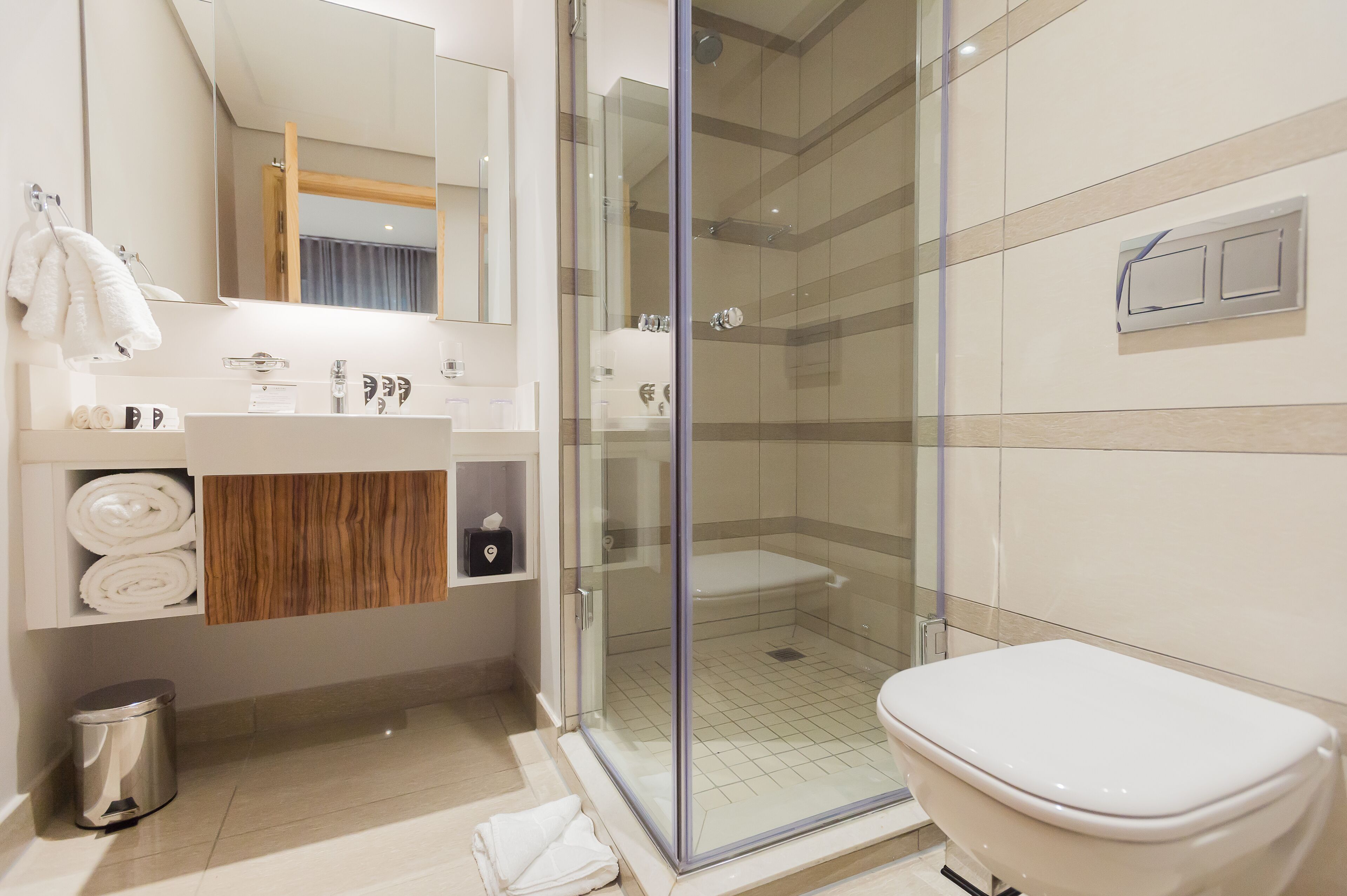 A modern bathroom with a glass-enclosed shower, a toilet, a sink with a wooden vanity, and a mirror.